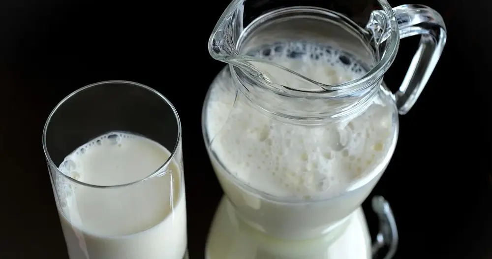 Copo e jarra de vidro com leite sobre fundo escuro, fonte alimentar de cálcio e vitamina D para os ossos