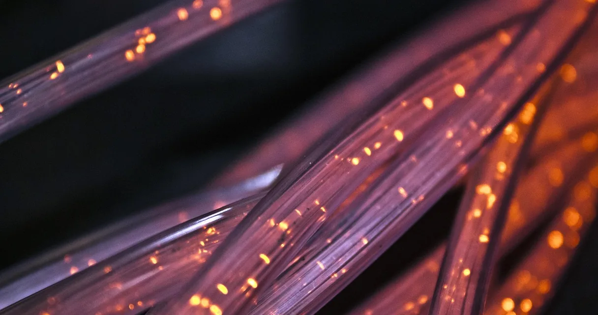 Fibras ópticas com pontos de luz em tons de roxo, ilustrando como ganhar dinheiro com IA