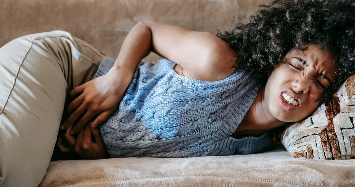 Mulher deitada no sofá com as mãos na barriga, com expressão de dor